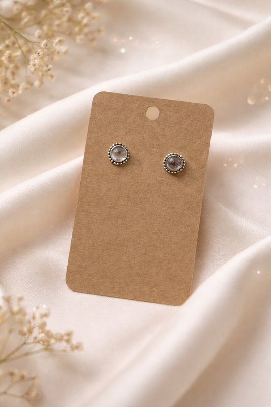 Clear stud earrings with silver tone setting displayed on a neutral card with a soft light background