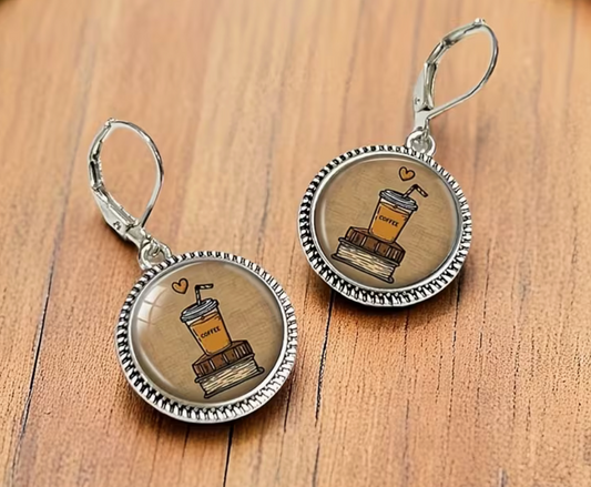 Pair of vintage-inspired silver-tone dangle earrings featuring round glass-look pendants with illustrations of iced coffee cups on stacks of books and small hearts.
