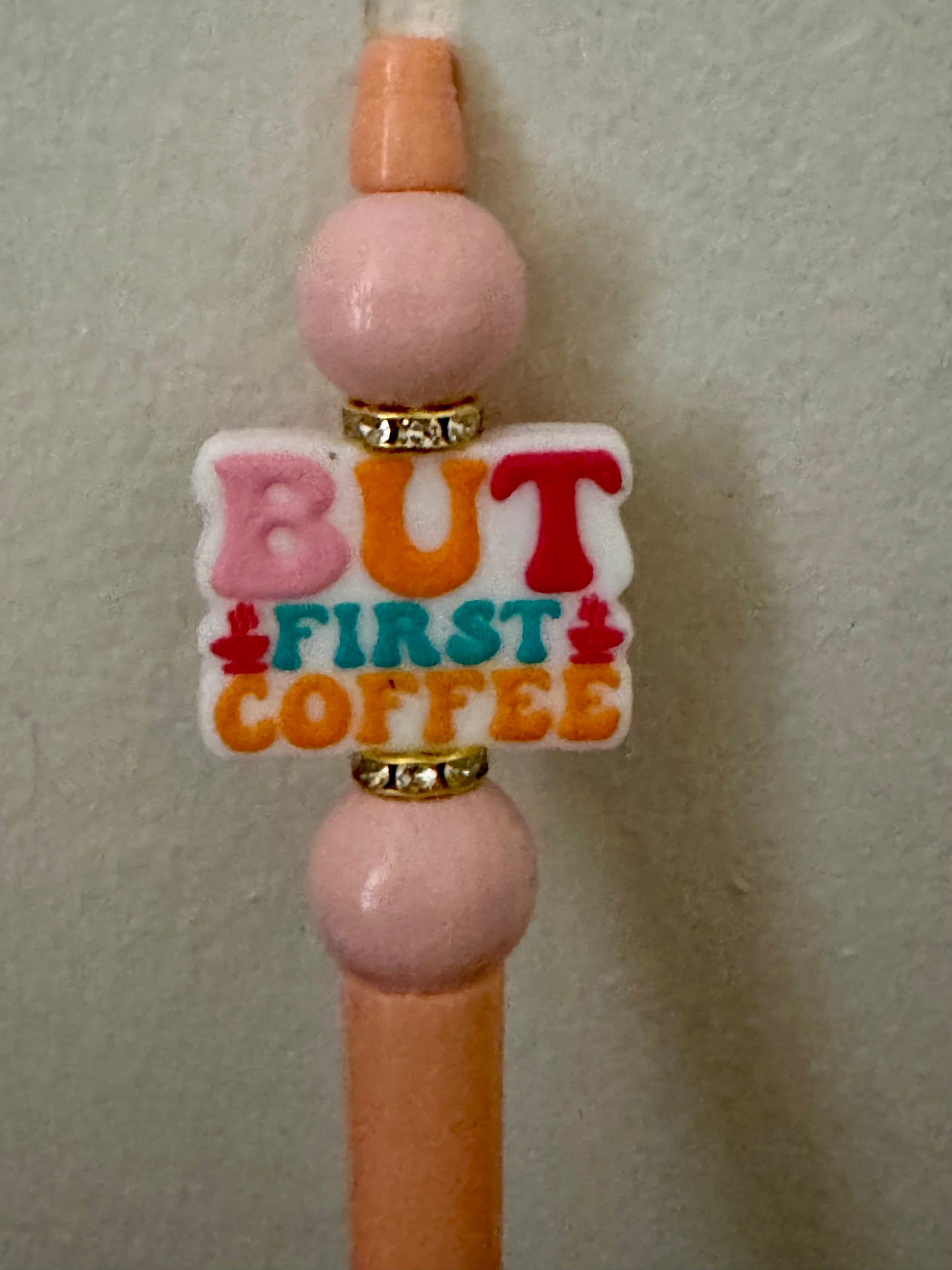 Decorative phone charm with 'But First Coffee' text on a plain background