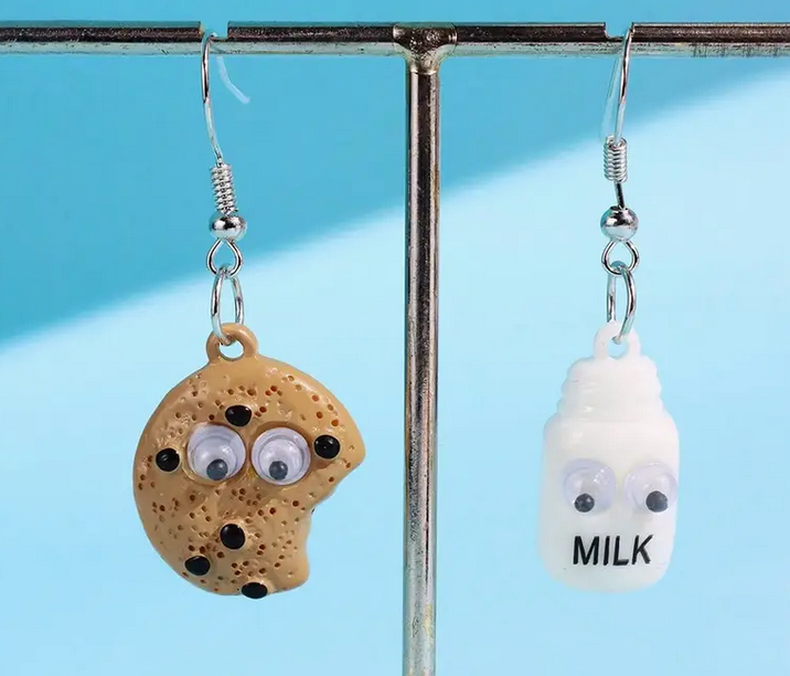 Cookie and milk earrings with googly eyes on a stand against a blue background