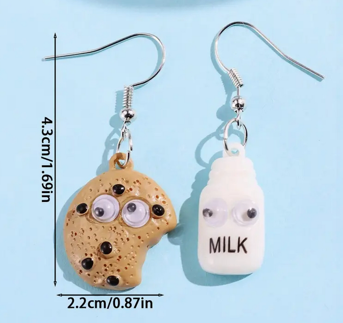 Pair of earrings shaped like a cookie and a milk bottle with googly eyes on a blue background.