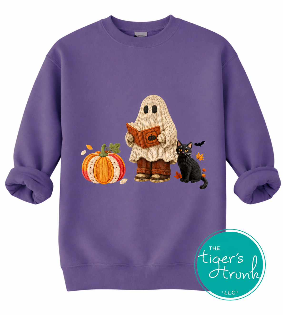 A purple crewneck sweatshirt featuring a Halloween graphic of a ghost reading a book, next to a pumpkin and a black cat. A teal circular logo for 'The Tiger's Trunk' is in the bottom right corner.