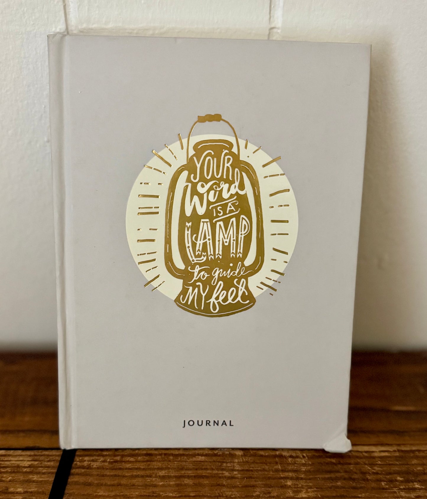 Journal with a decorative cover featuring text and a lamp illustration on a wooden surface.