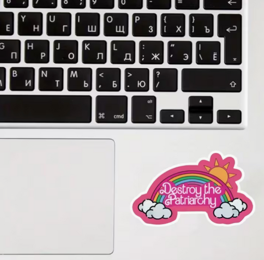 Colorful Destroy the Patriarchy rainbow sticker displayed on a laptop beside a keyboard and trackpad