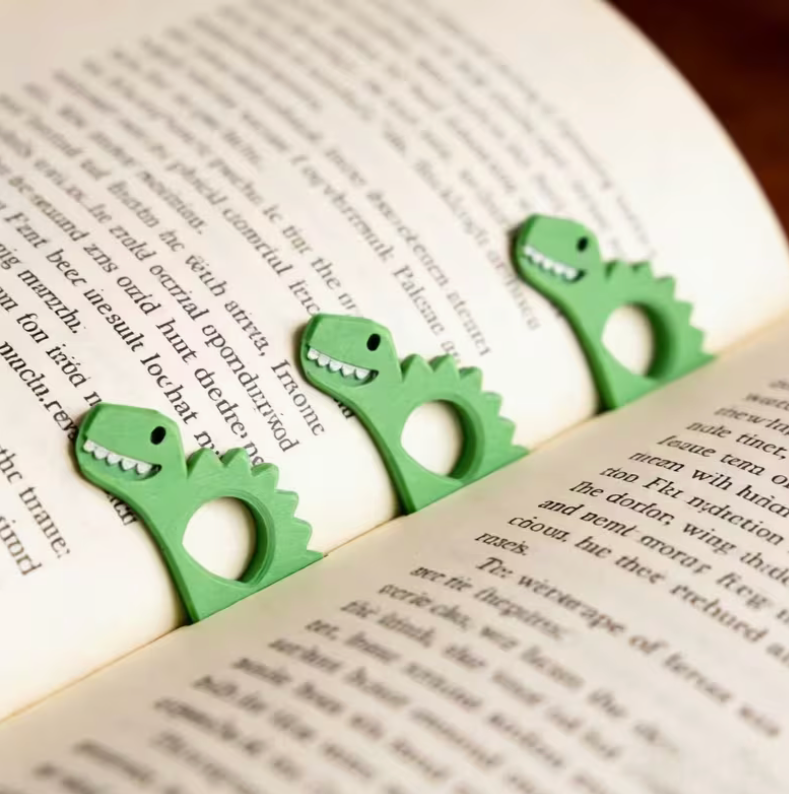 green dinosaur thumb bookmarks holding pages open inside an open book