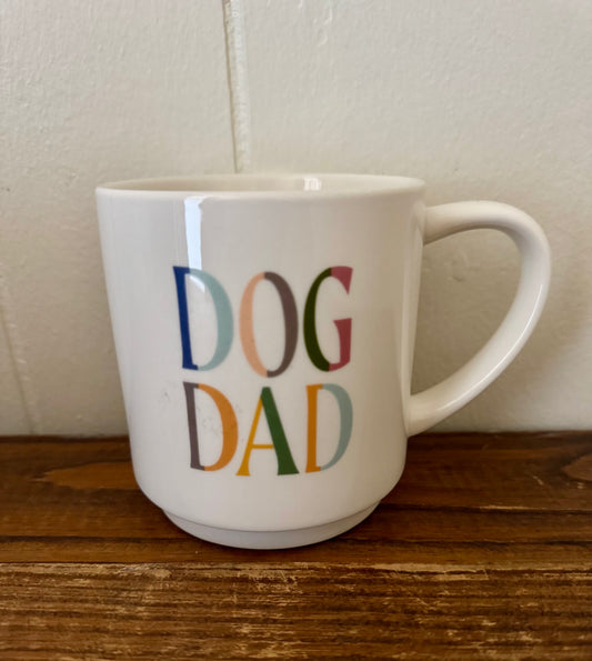 White mug with 'DOG DAD' in colorful letters on a wooden surface.