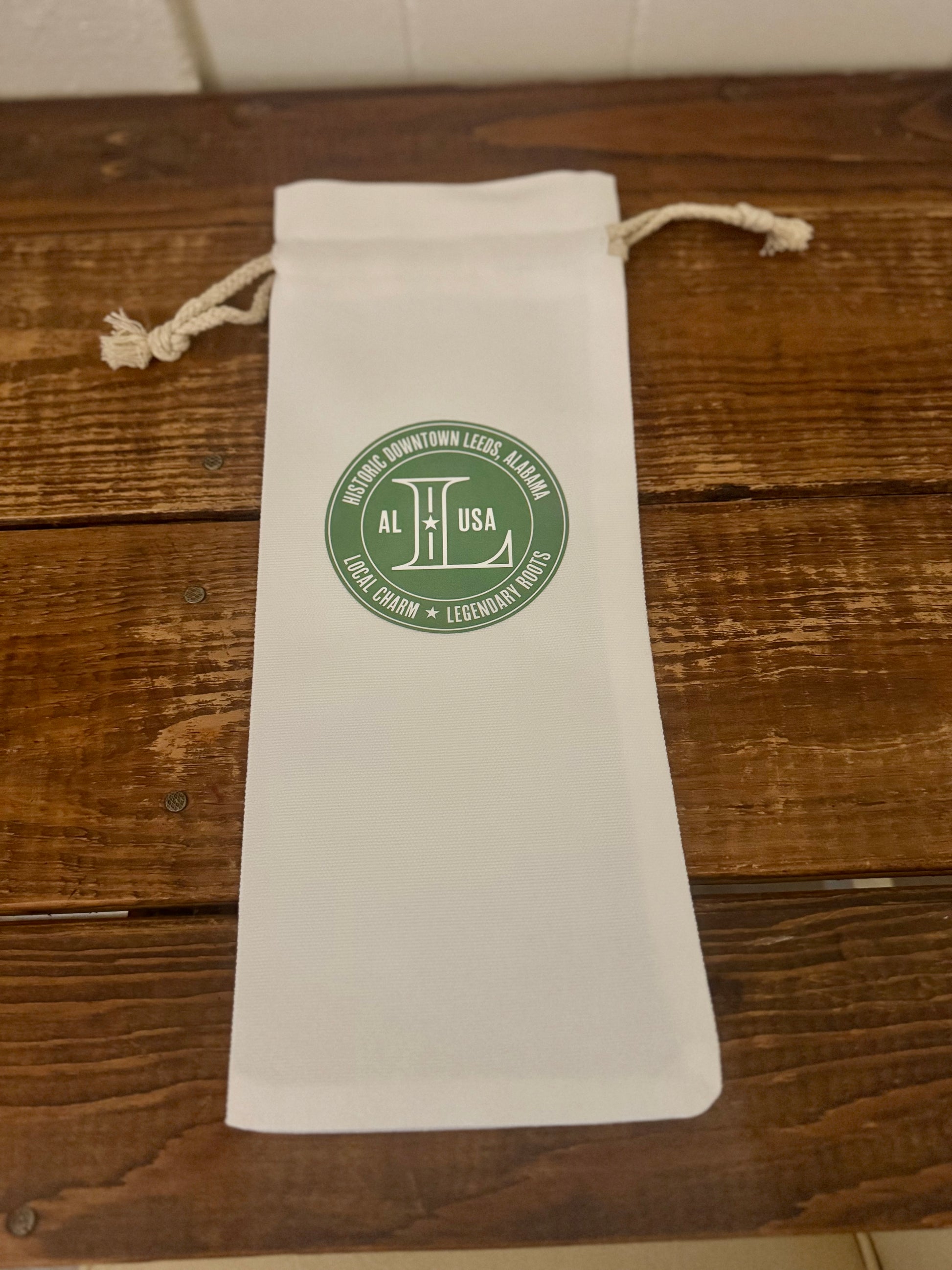 White drawstring bag with a green logo on a wooden surface