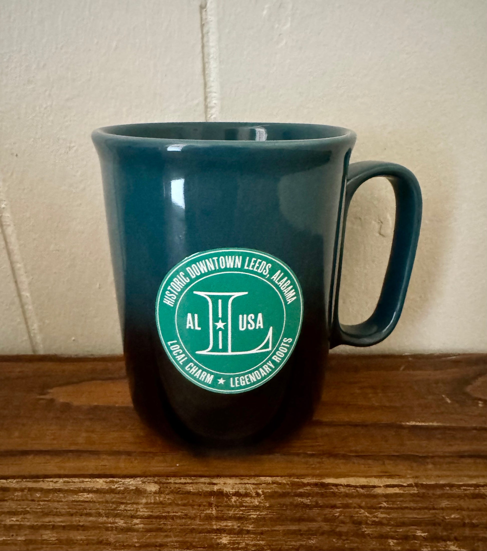 Blue mug with a green logo on a wooden surface