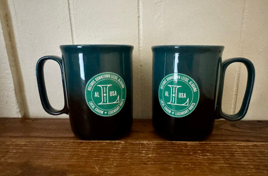 Two black mugs with a green logo on a wooden surface.