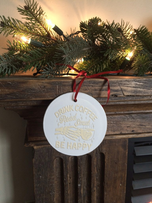 Ceramic ornament reading Drink Coffee Read Smut Be Happy hanging by red ribbon