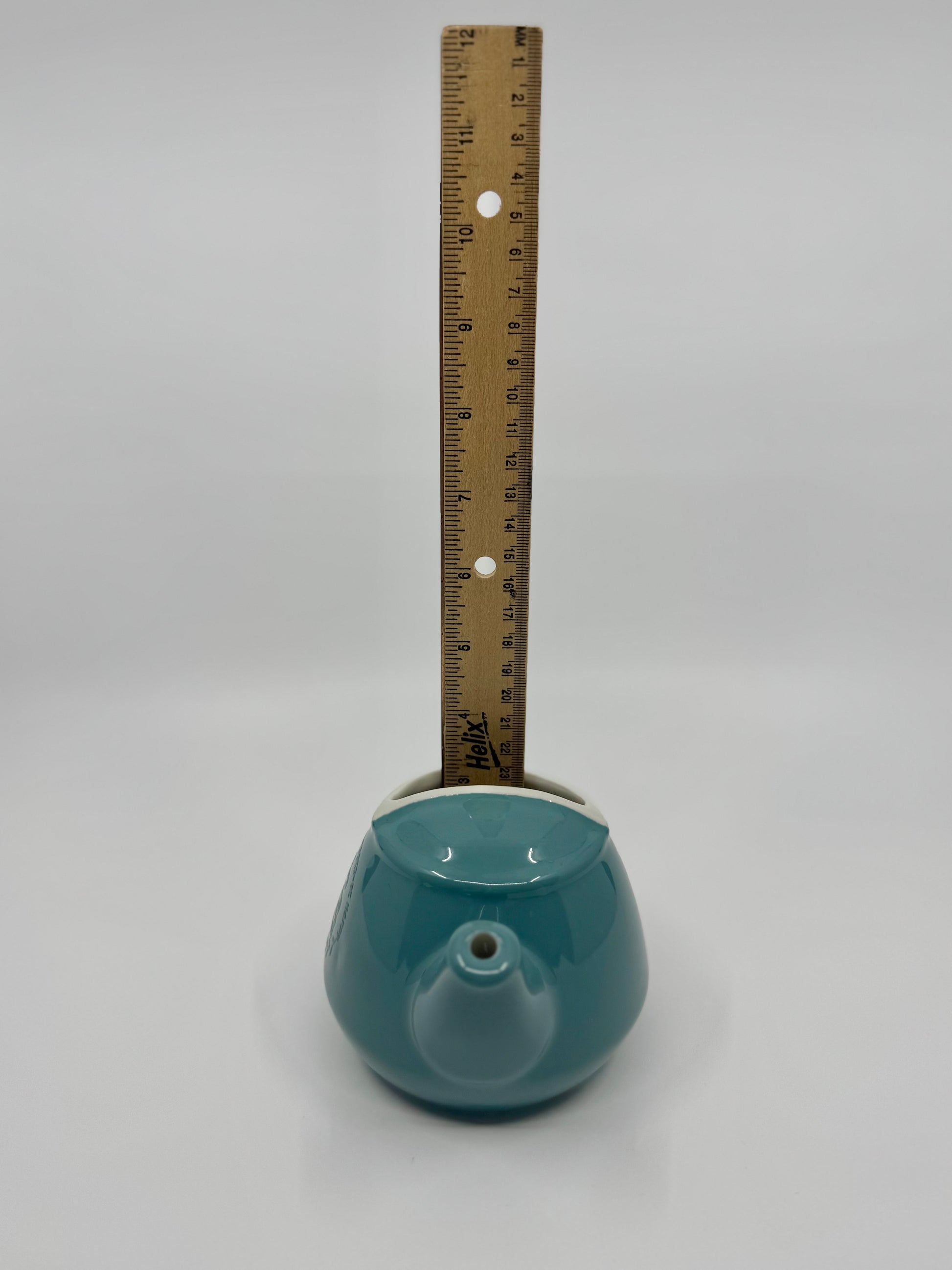 Teal ceramic object with a ruler for scale on a gray background