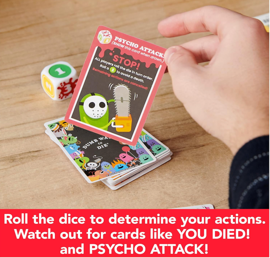 Player holding a Psycho Attack card from the Dumb Ways to Die card game beside the oversized die and colorful game cards