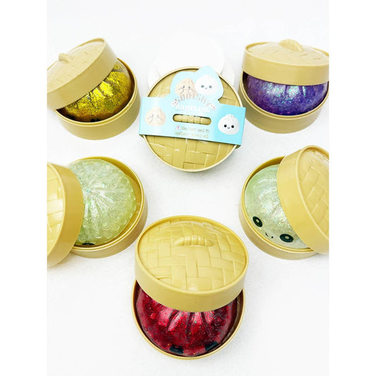 Glitter dumpling squishy toy inside a bamboo-style steamer container with assorted colorful squishies including green, red, purple, and gold