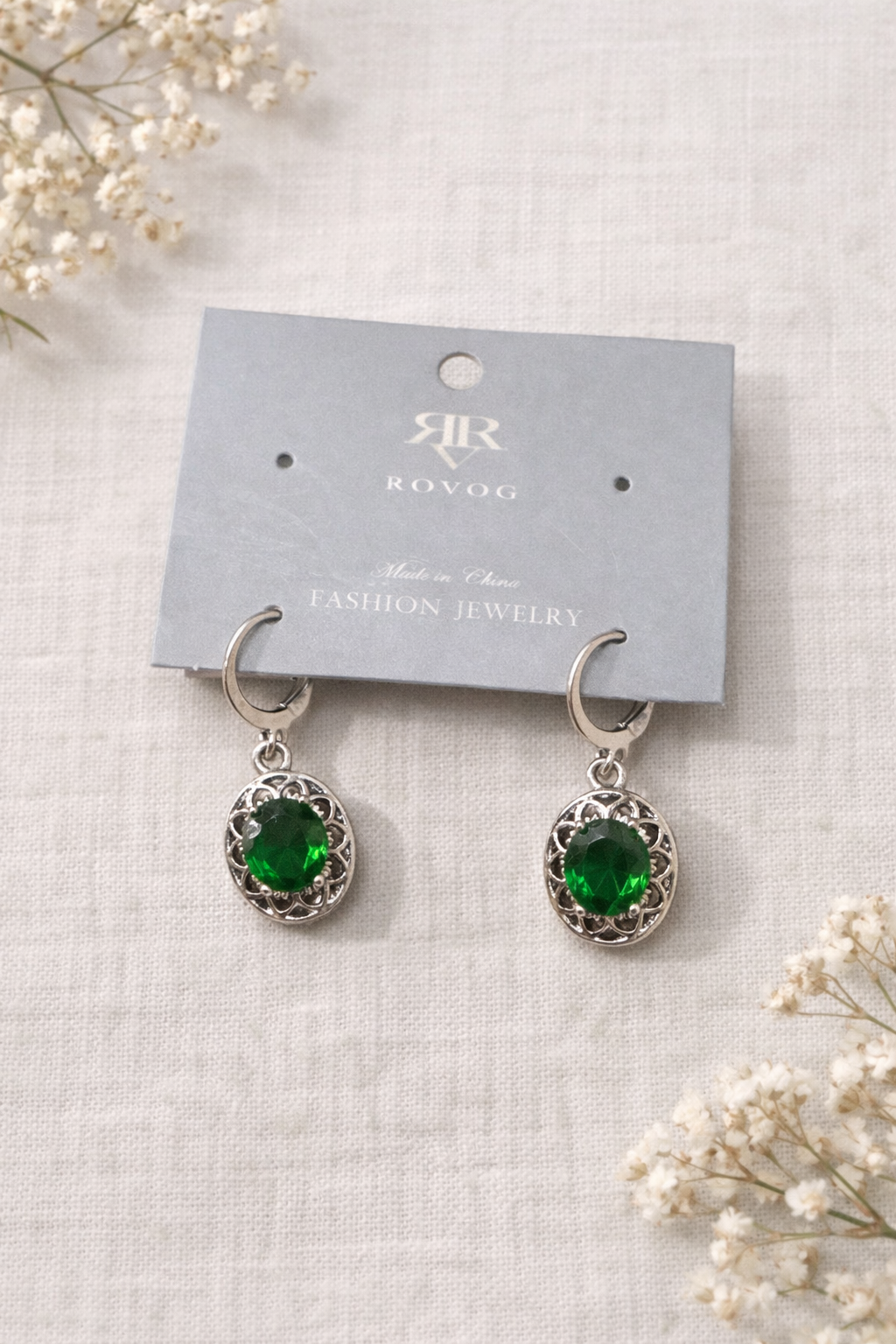 Egg shaped green drop earrings with ornate silver tone setting displayed on a jewelry card