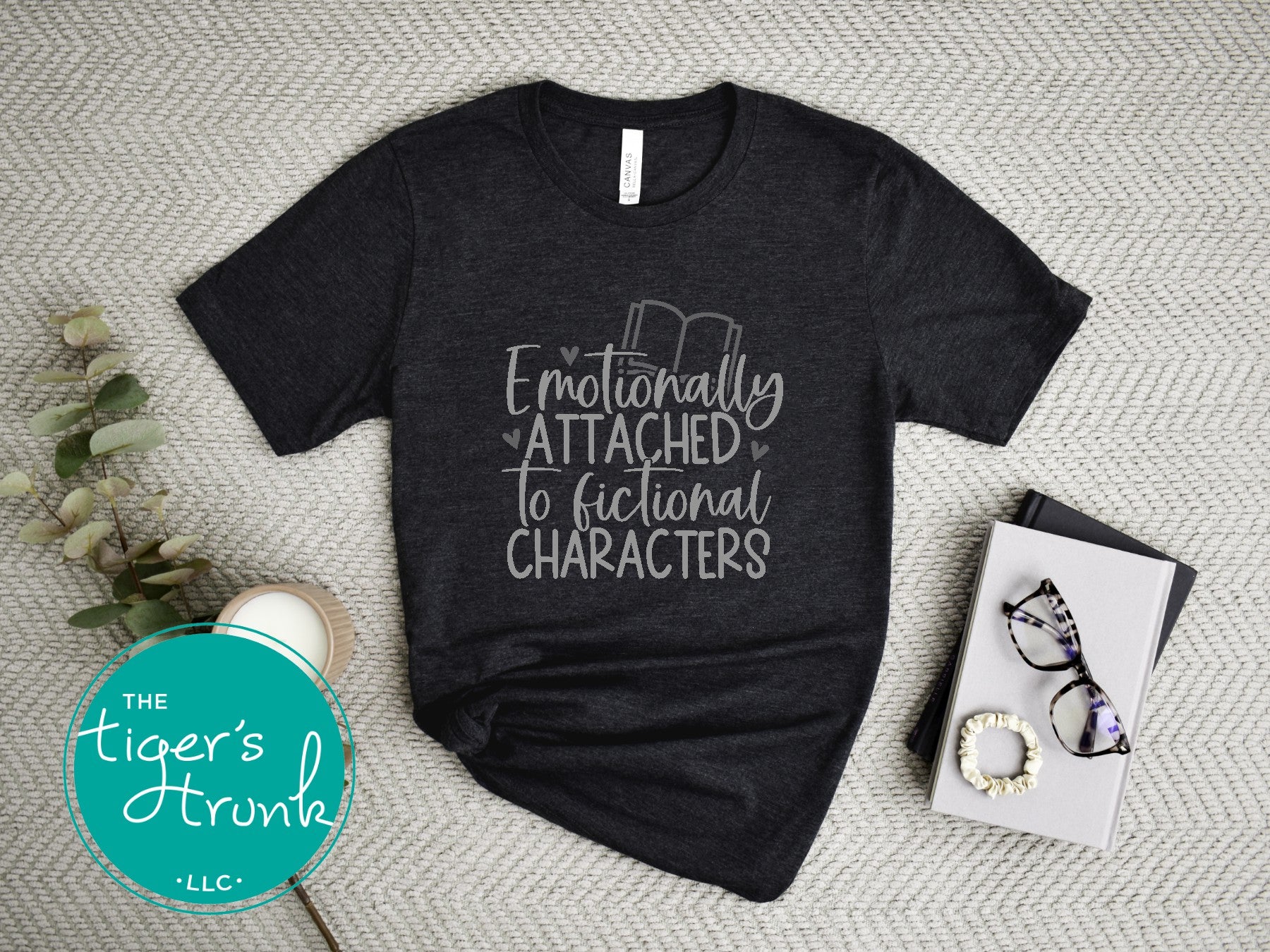 Black t-shirt with 'Emotionally Attached to Fictional Characters' text on a textured surface with 'The Tiger's Trunk' logo.