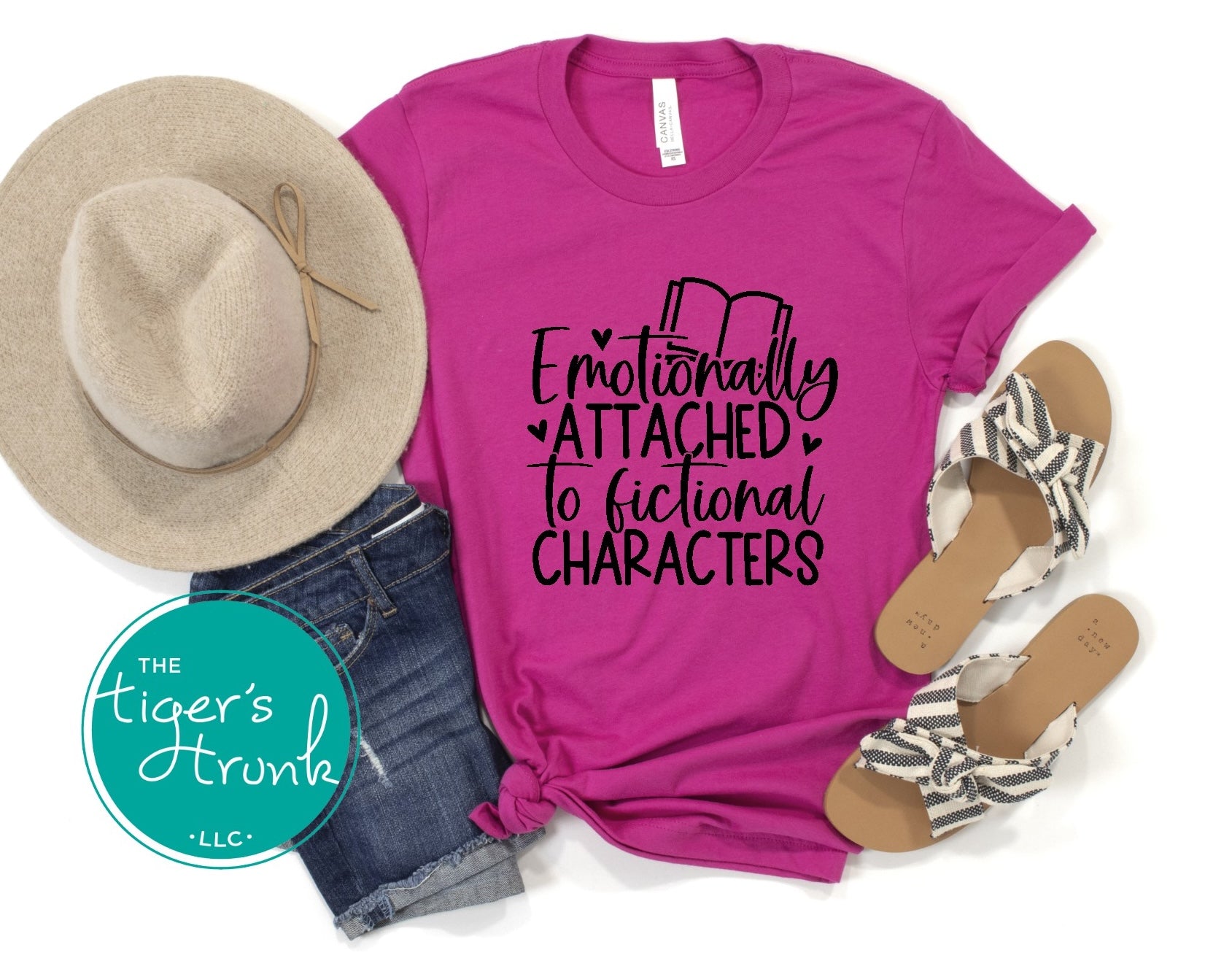 Pink t-shirt with 'Emotionally Attached to Fictional Characters' text, hat, denim shorts, and sandals on a white background.