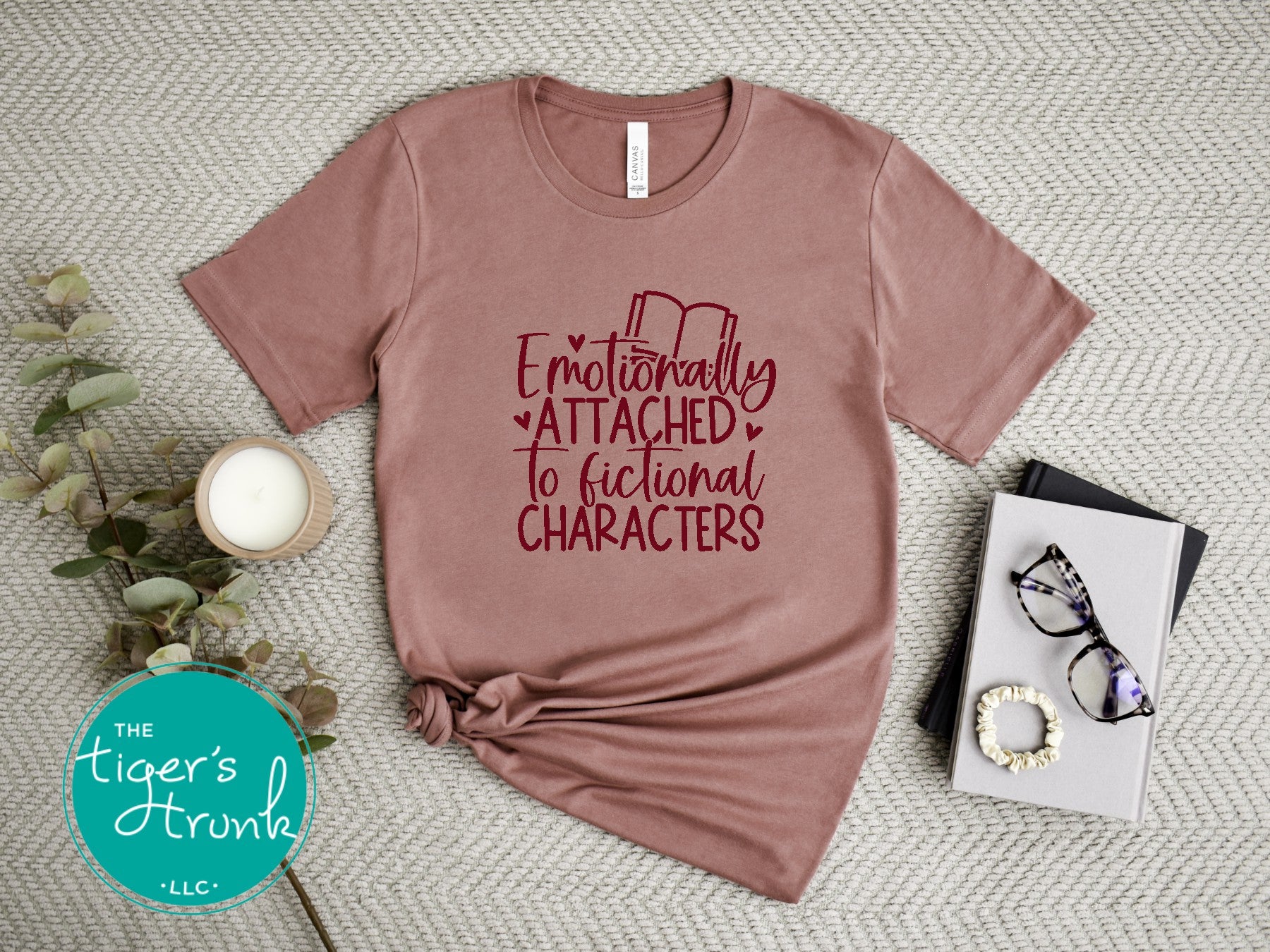 Mauve t-shirt with red text 'Emotionally Attached to Fictional Characters' on a textured surface with decor items.