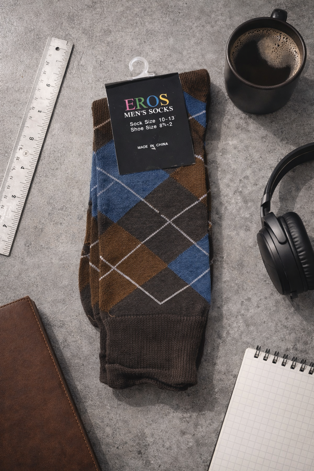 EROS men’s argyle crew socks in brown and blue diamond pattern with retail hang tag showing sock size 10–13 and men’s shoe size 8½–12, styled in a modern work desk flatlay with coffee mug, headphones, ruler, notebook, and leather notebook.