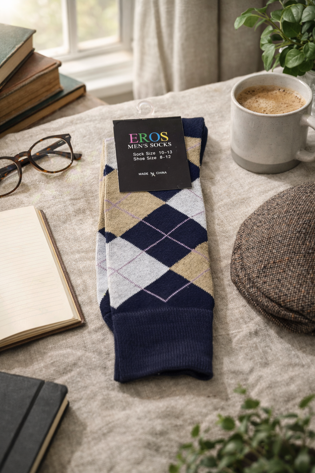 EROS men’s argyle crew socks in navy blue, cream, and tan diamond pattern with retail hang tag showing sock size 10–13 and men’s shoe size 8–12, styled in a cozy desk flatlay with books, notebook, glasses, coffee mug, and hat near a window.