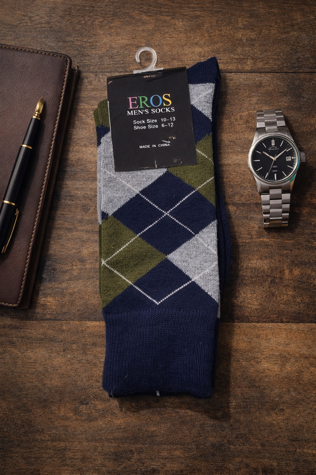 EROS men’s argyle crew socks in navy blue, olive green, and gray diamond pattern with retail hang tag showing sock size 10–13 and men’s shoe size 6–12, styled on a wooden desk flatlay with a leather notebook, fountain pen, and silver wristwatch.