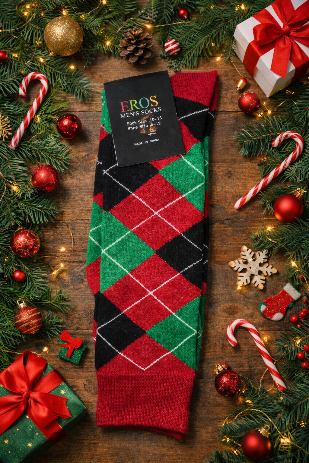 EROS men’s argyle crew socks in red, green, and black diamond pattern with retail hang tag showing sock size 10–13 and men’s shoe size 6–12, styled in a Christmas flatlay with evergreen branches, ornaments, candy canes, and gift boxes on a wooden background.