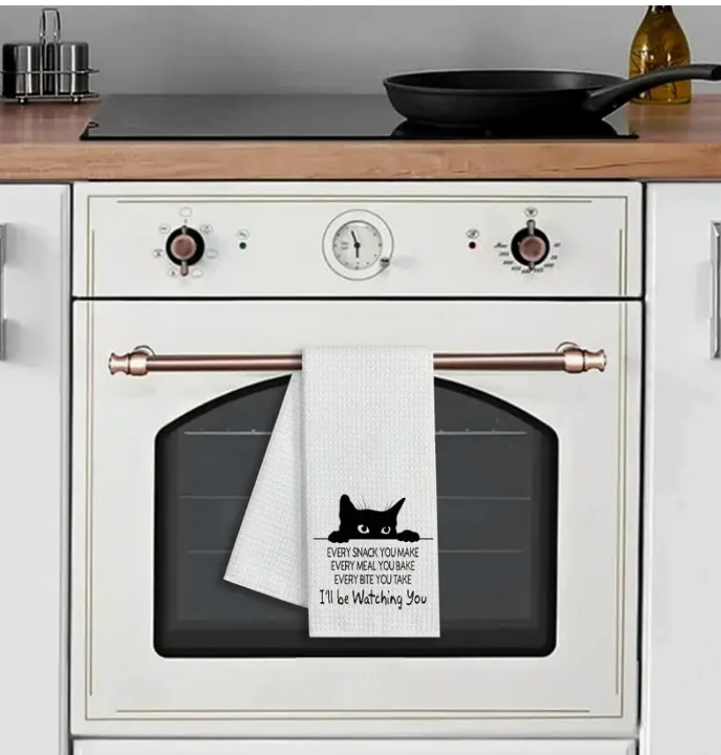 White oven with a black cat design towel hanging on the handle in a kitchen setting.
