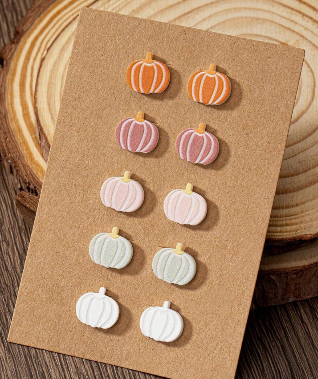 Set of pumpkin-shaped earrings on a brown card with a wooden background