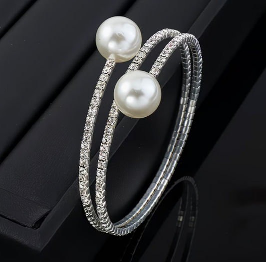 Silver tone multilayer bangle bracelet with faux pearls and rhinestone rows on dark background