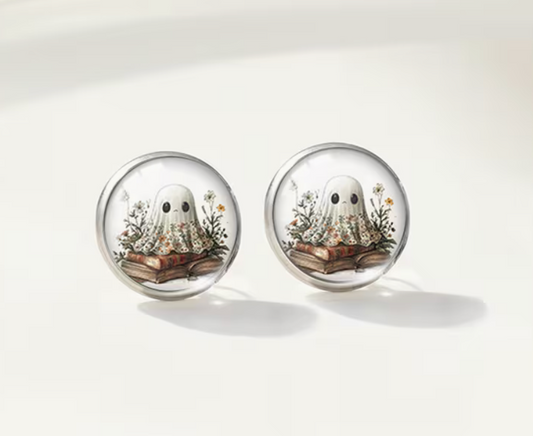 Round glass stud earrings featuring a cute white ghost sitting on vintage books surrounded by delicate wildflowers