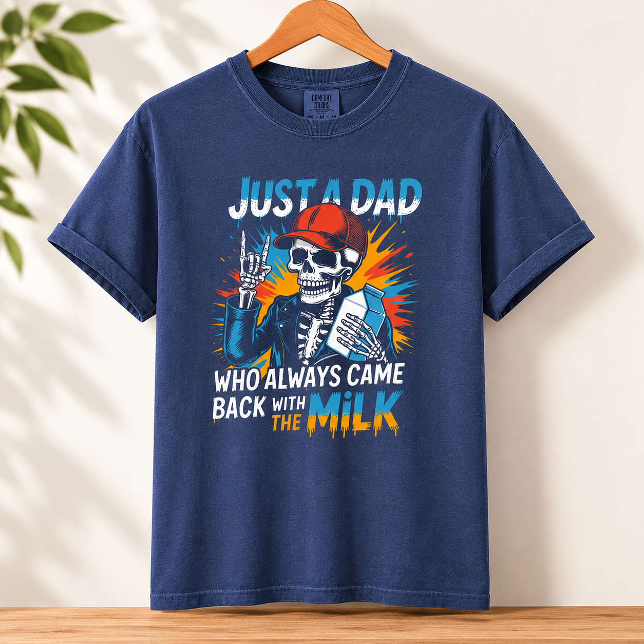 Blue graphic t-shirt featuring skeleton holding milk carton with humorous dad joke phrase and colorful retro-inspired artwork