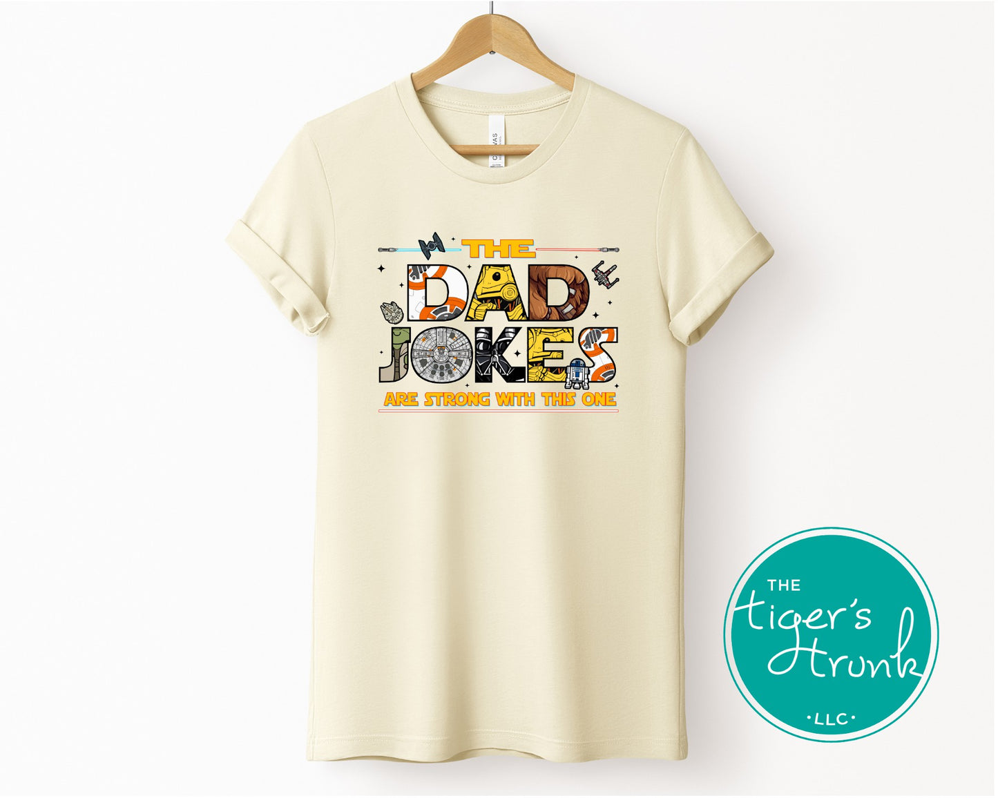 Natural cream colored t-shirt featuring colorful retro-inspired dad jokes graphic with space and galaxy themed elements hanging on wooden hanger