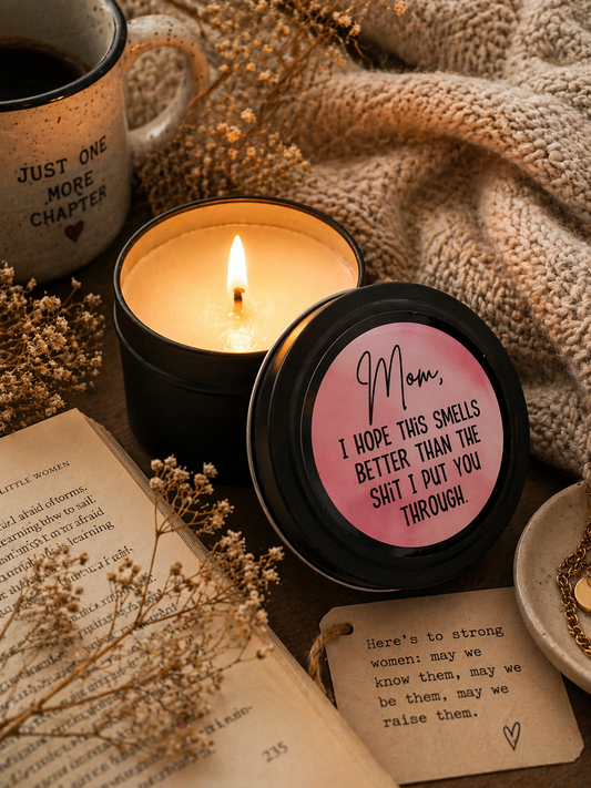 Candle with a humorous label next to an open book and coffee cup
