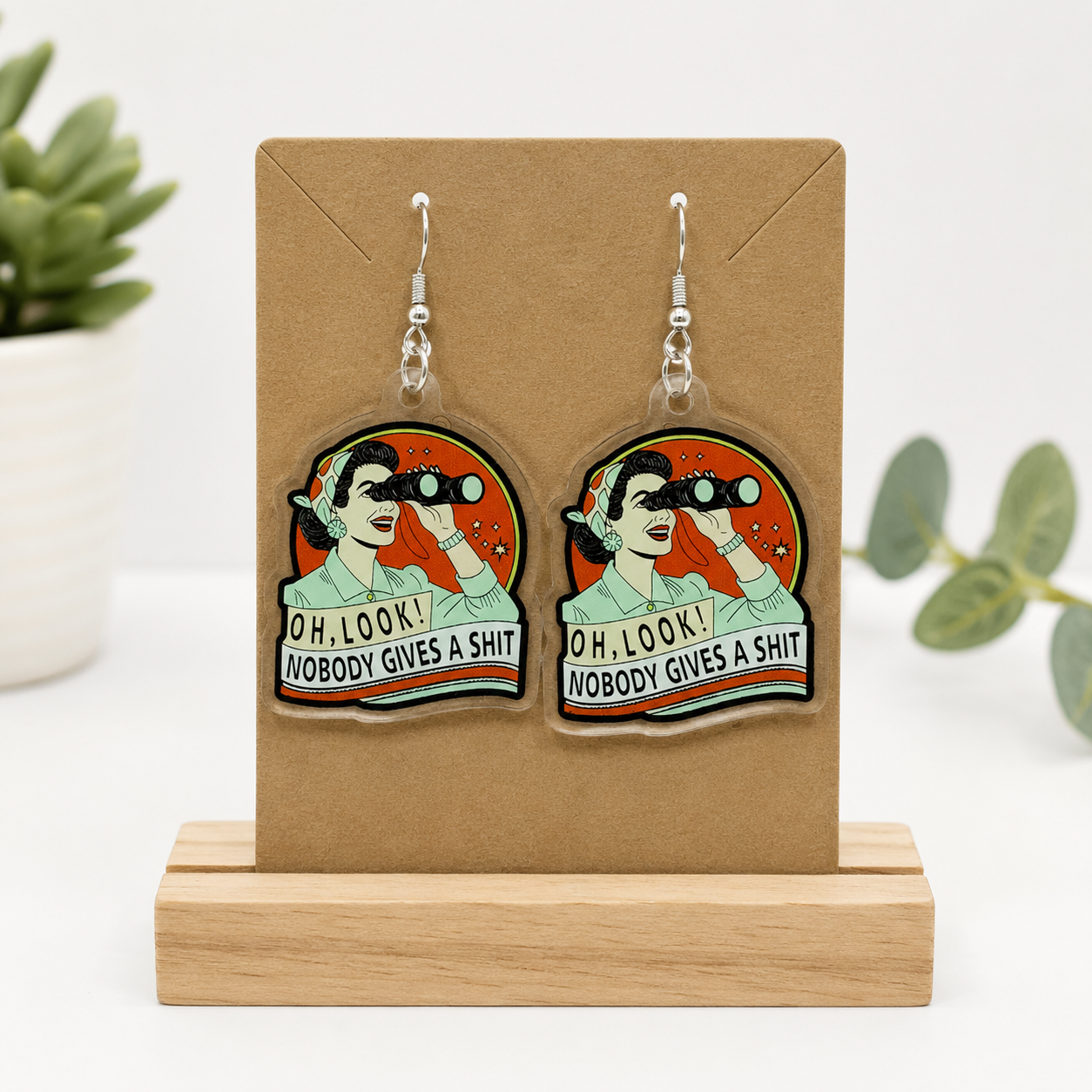 Lightweight acrylic dangle earrings featuring a retro cartoon woman with binoculars and the humorous phrase Oh, Look! Nobody Gives a Shit.