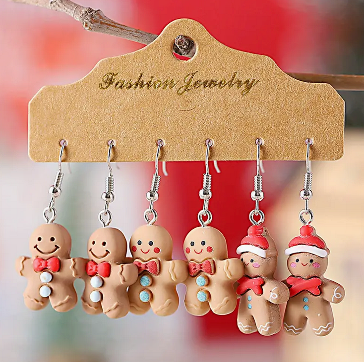 Set of gingerbread man earrings on a 'Fashion Jewelry' hanger with a blurred red background.