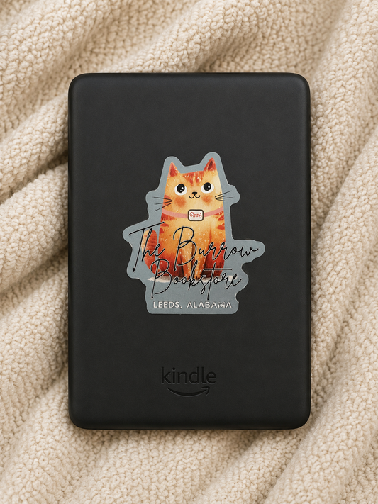 Sage green Ginny the bookstore cat die cut sticker featuring The Burrow Bookstore logo displayed on a Kindle resting on a cozy cream blanket.