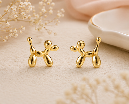 Gold balloon dog stud earrings with polished balloon animal design displayed on a neutral background with soft floral accents