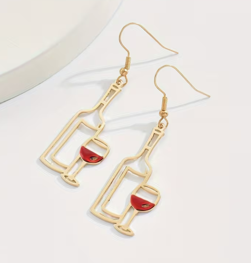 Closeup of gold wine bottle and wine glass earrings with red enamel wine detail.