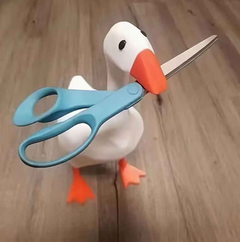 whimsical resin goose figurine holding blue scissors in its beak on wooden floor surface