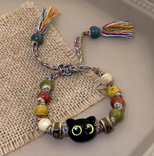 Colorful beaded bracelet with a black cat charm on a textured surface