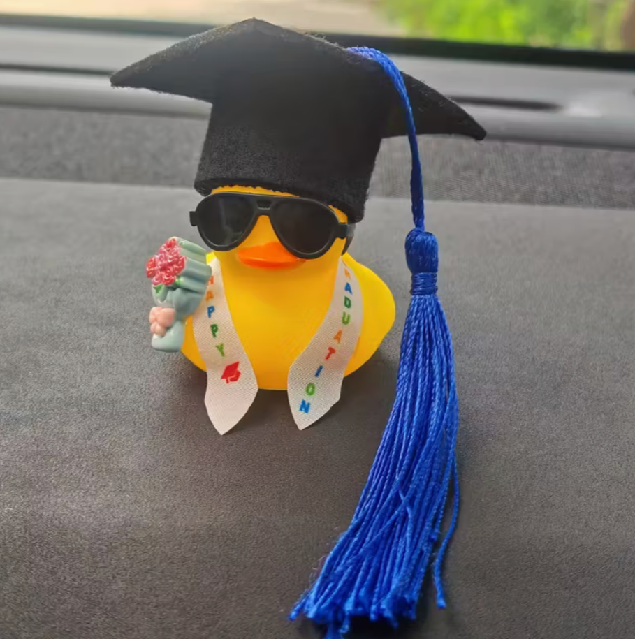 Graduation-themed rubber duck with a blue tassel on a car dashboard