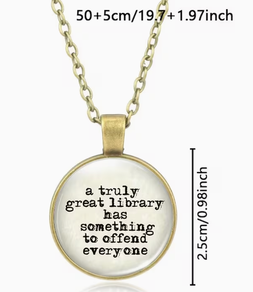 A round pendant necklace with a gold-toned chain and bezel, featuring the printed quote 'a truly great library has something to offend everyone' in black text on a white background. The image includes size text at the top ('50+5cm/19.