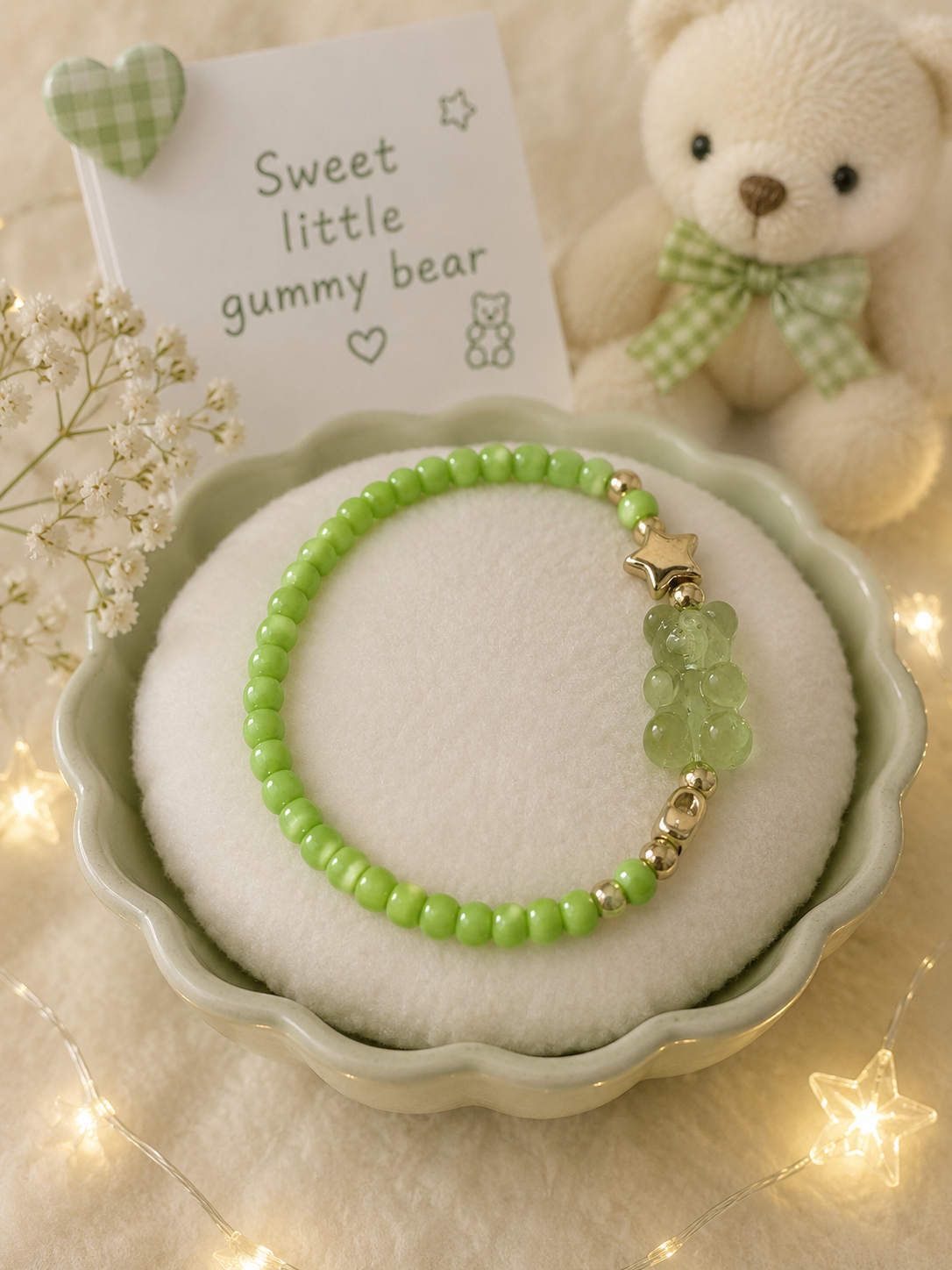 Green stretch bead bracelet with transparent gummy bear charm and gold accents displayed in pastel dish