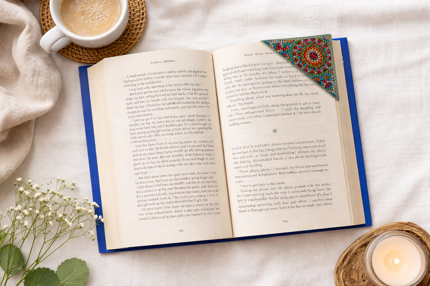 Open book styled on neutral linen with coffee, candle, and bejeweled vegan leather corner bookmark for reading aesthetic