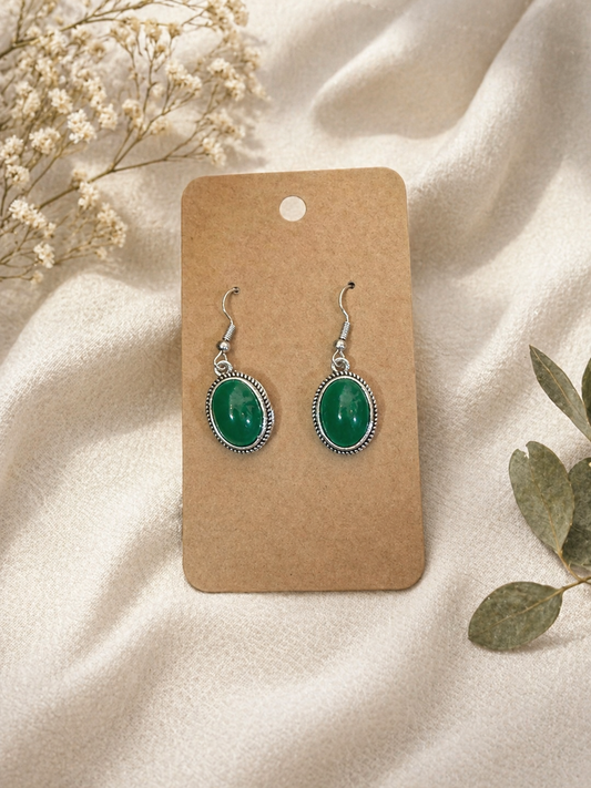 Green oval stone dangle earrings with silver-tone setting displayed on kraft jewelry card with neutral fabric background