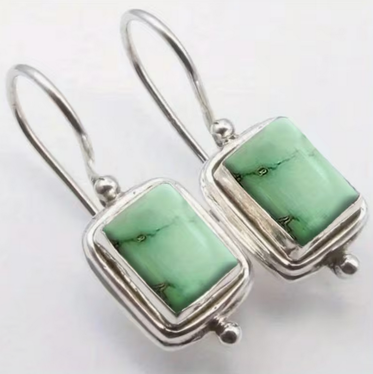Silver dangle earrings with rectangular green stone settings and simple hook backs on a white background
