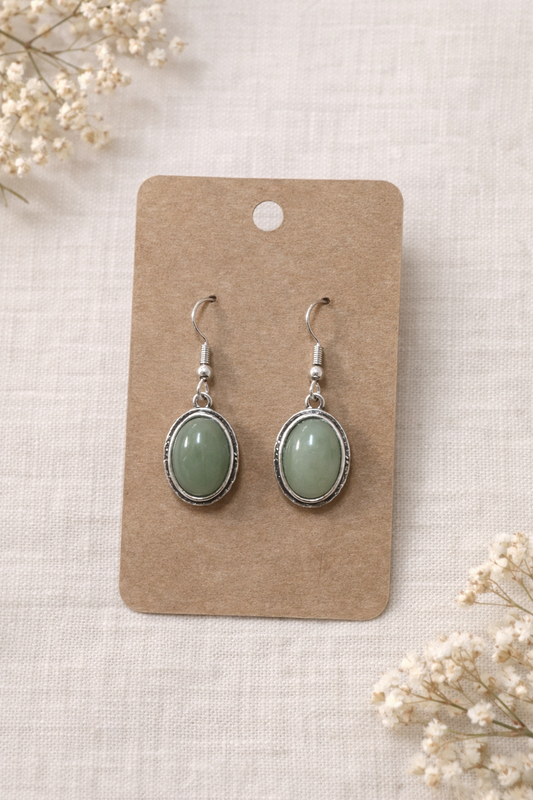 Green teardrop earrings with silver tone hooks displayed on a neutral jewelry card