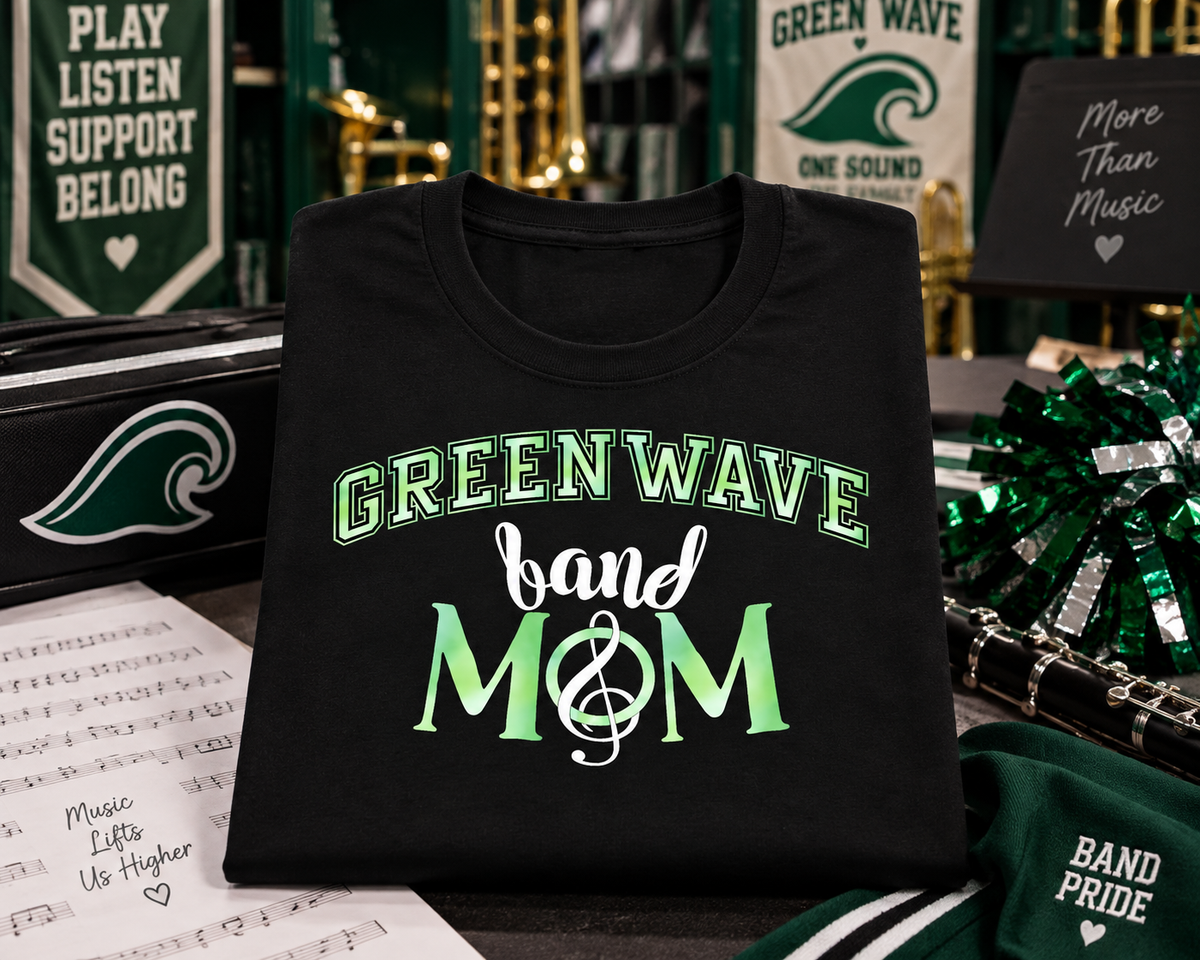 A black short-sleeve T-shirt with 'GREENWAVE band MOM' printed on the front in green and white, styled on a tabletop with music-themed props and Green Wave branding in the background.