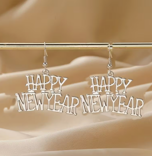 Gold Happy New Year dangle earrings hanging from a display bar against a soft fabric background.