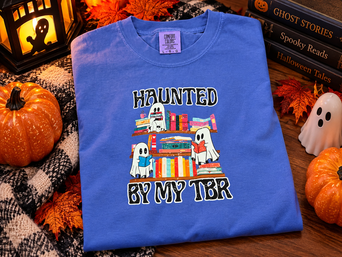 Blue Comfort Colors T-shirt featuring Haunted by My TBR Halloween design with cute white ghosts reading books beside colorful bookshelves.