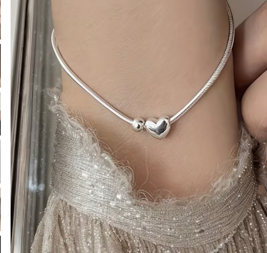 Close up of dainty heart charm bracelet worn on wrist with silver chain